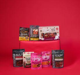Assorted dog treats in colorful packaging displayed on a red surface against a red background.