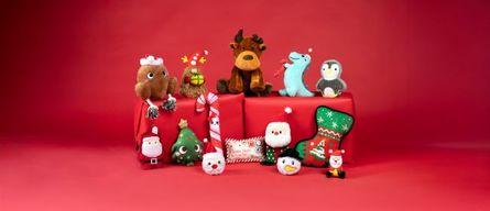 A collection of festive plush toys, including a reindeer, penguin, and Santa, arranged on red gift boxes against a red background.