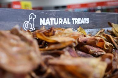 Close-up of a display of natural dog treats, with a sign featuring a dog icon and the words "Natural Treats" in a pet store.